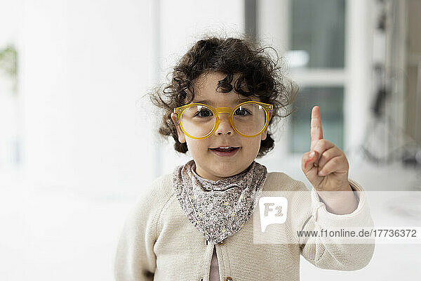 Cute little girl wearing oversized eyeglasses raising finger