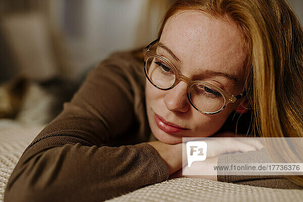 Sad woman wearing eyeglasses lying on bed at home