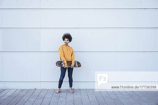 Young woman holding skateboard standing in front of wall