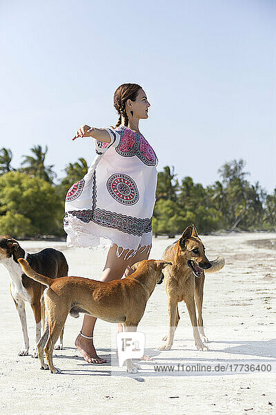Woman with arms outstretched standing by dogs at beach