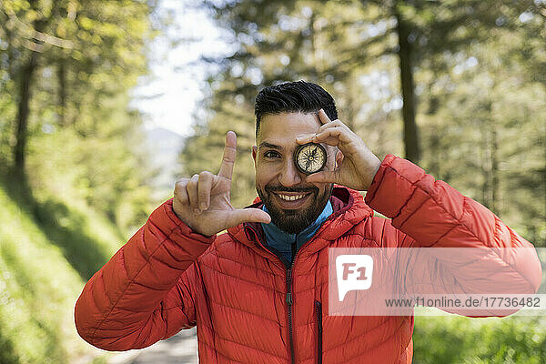 Happy man covering eye with navigational compass