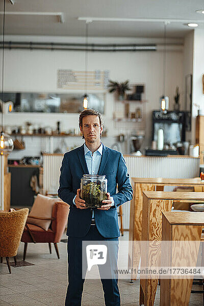 Reifer Geschäftsmann mit Pflanze im Glasbehälter steht im Café