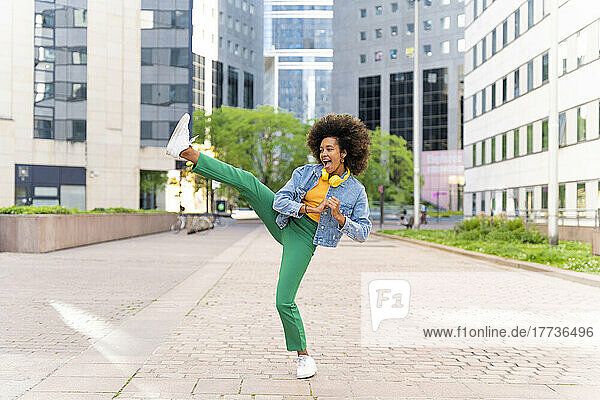 Happy woman with Afro hairstyle kicking on footpath
