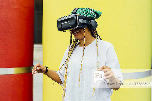 Happy woman wearing virtual reality simulator standing in front of yellow concrete pipe