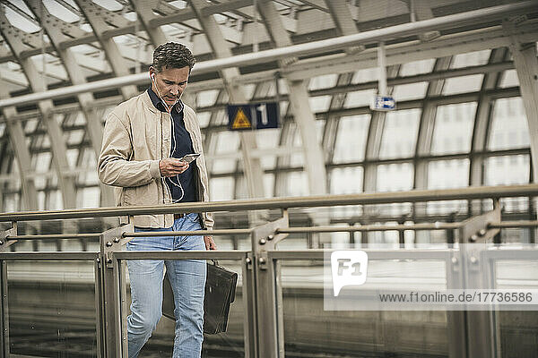 Mature businessman using smart phone walking with bag at railroad station