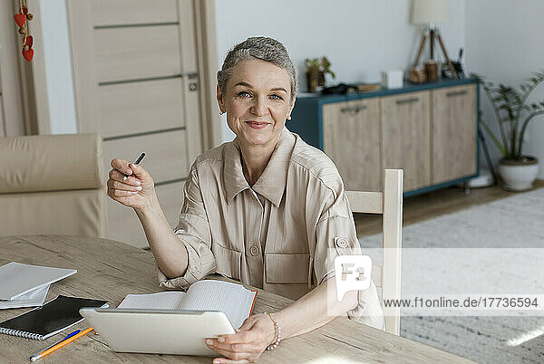 Portrait of woman using digital tablet and taking notes at table at home