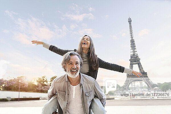Happy mature man giving piggyback ride to woman in front of Eiffel Tower  Paris  France