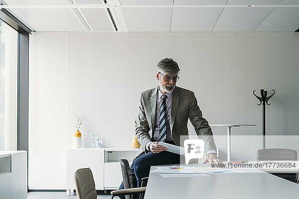 Businessman sitting with tablet PC analyzing documents on desk in office