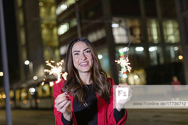 Happy woman with sparklers standing on street at night