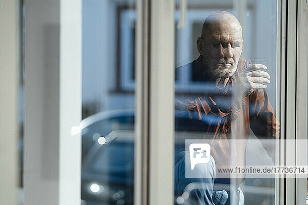 Businessman holding drinking glass in office seen through window