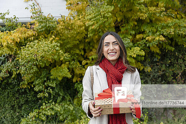 Happy beautiful woman with Christmas present standing in park