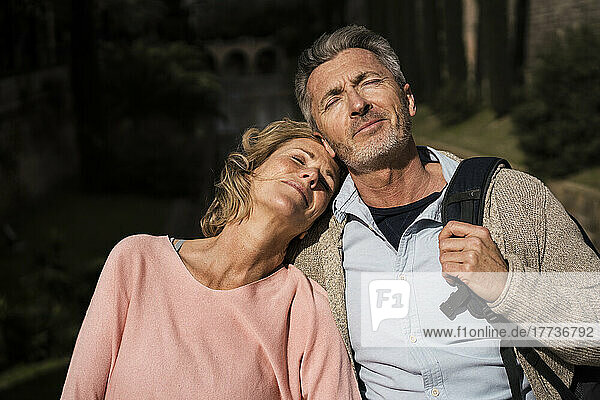 Mature woman leaning head on man's shoulder at sunny day
