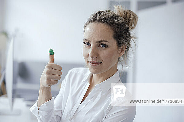 Businesswoman showing green color on thumb in office