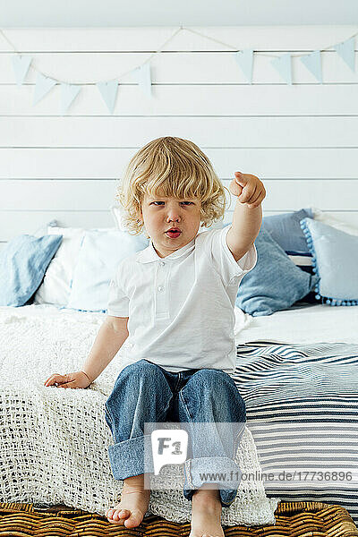 Boy gesturing with finger sitting on bed at home