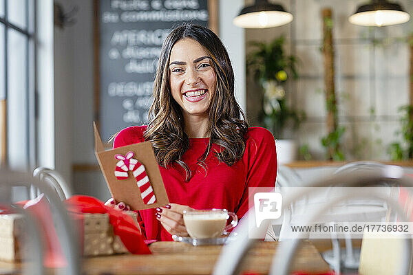 Cheerful woman with Christmas card sitting at table in cafe