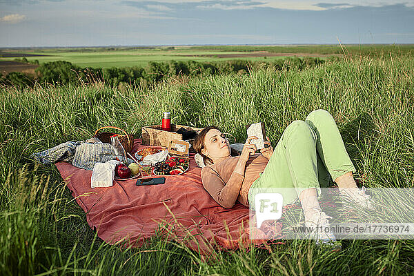 Smiling woman reading book at picnic in field