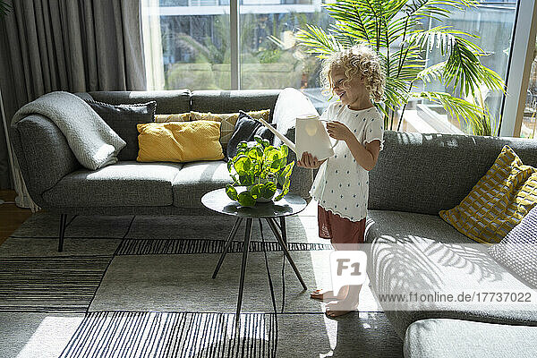 Cute girl watering plant in living room at home