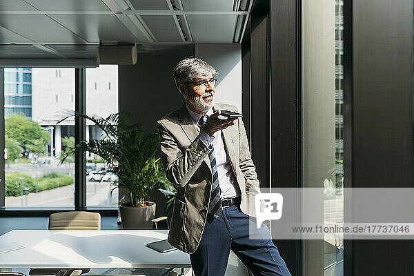 Businessman talking on smart phone standing by window in office