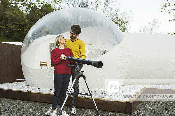 Glückliches Paar mit Teleskop vor transparentem Kuppelhotel