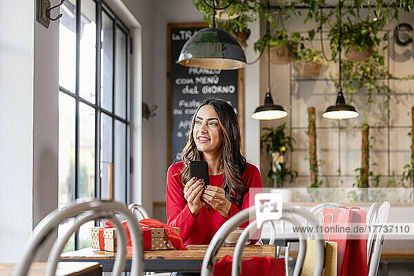 Smiling woman sitting with smart phone at table in cafe