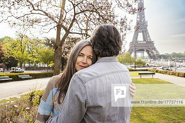 Smiling mature woman hugging boyfriend in front of Eiffel tower  Paris  France