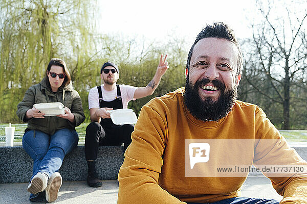 Smiling man spending leisure time with friends in background at park