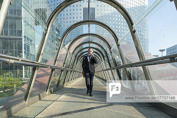 Mature businessman talking through mobile phone walking on footbridge
