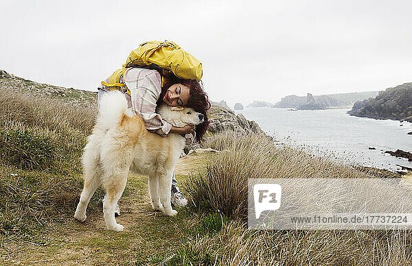 Smiling woman wearing backpack hugging pet dog