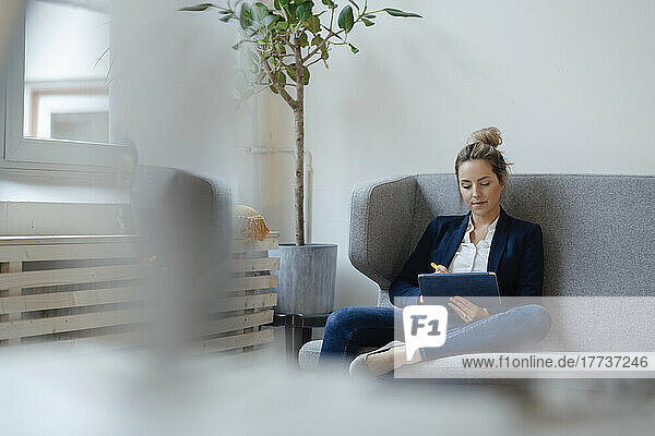 Businesswoman using tablet PC sitting on sofa in office
