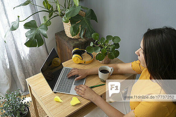 Woman with coffee mug using laptop at desk in home office