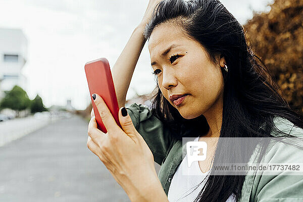 Young woman adjusting hair looking at smart phone