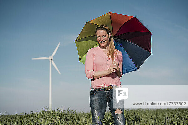 Smiling woman standing with colorful umbrella in field on sunny day