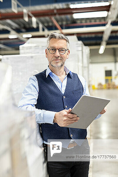 Manager wearing eyeglasses standing with tablet PC by box in warehouse