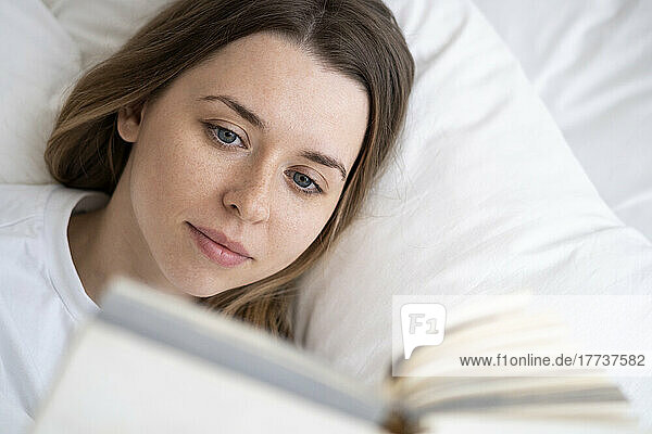 Beautiful woman reading book lying on bed at home