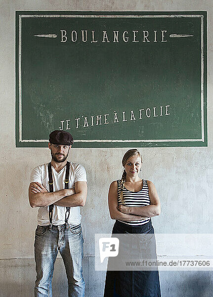 Confident bakery owners standing with arms crossed in front of wall with French text