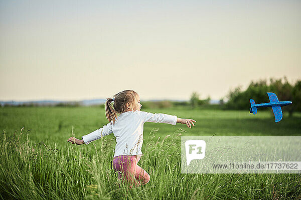 Playful girl throwing airplane in agricultural field