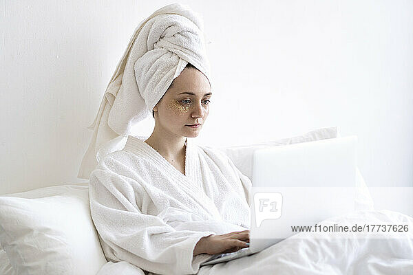 Frau im Bademantel benutzt Laptop zu Hause im Bett