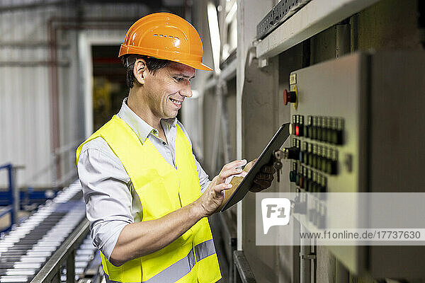 Smiling worker using tablet PC by control panel in warehouse