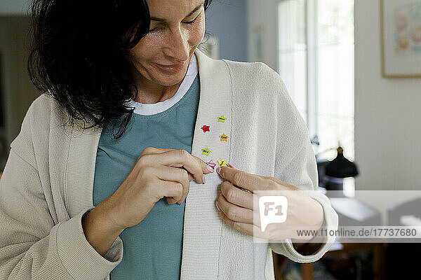 Smiling woman adjusting star shape stickers on cardigan sweater at home
