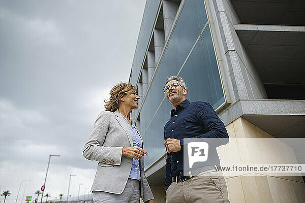 Smiling businessman discussing with businesswoman standing in front of office building