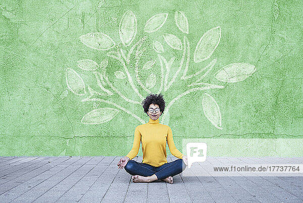Young woman meditating under tree painted on wall