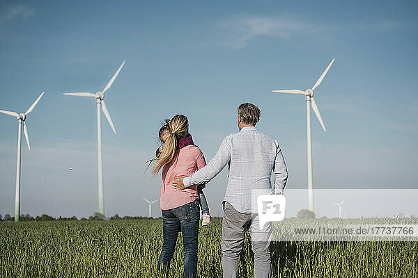 Woman carrying daughter standing by man at wind farm on sunny day