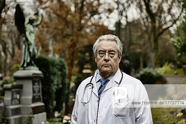 Senior doctor wearing lab coat standing on cemetery