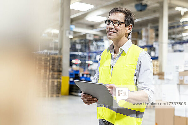 Smiling worker with tablet PC standing in warehouse
