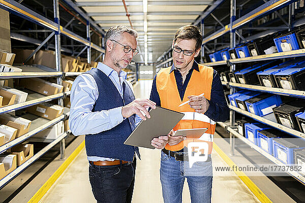 Manager discussing over tablet PC with worker in aisle at warehouse