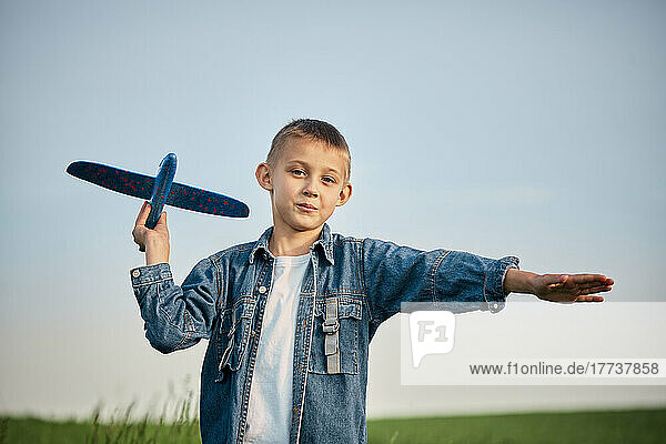 Netter Junge spielt mit Spielzeugflugzeug vor dem Himmel bei Sonnenuntergang