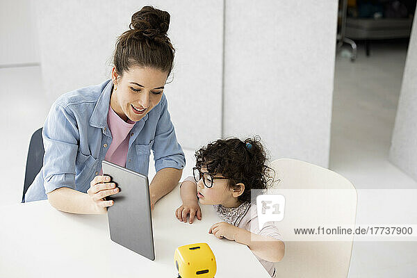 Working mother sitting at table daughter playing with AI toy robot