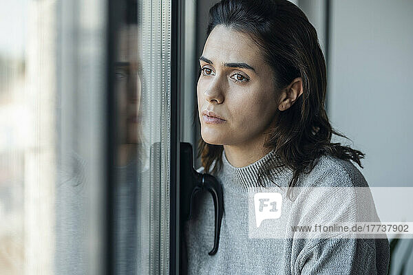 Sad woman looking out through window at home