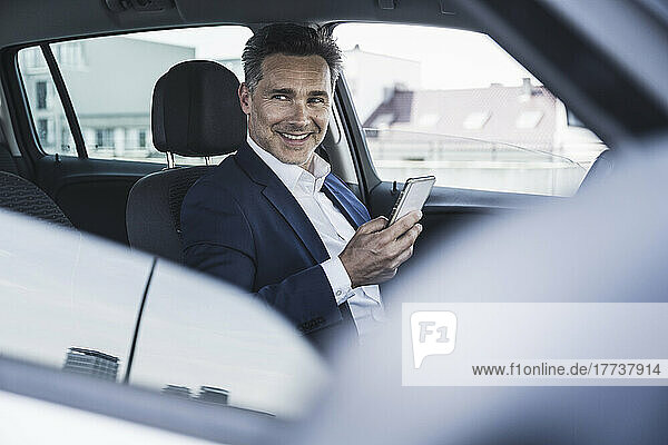 Smiling businessman sitting with smart phone in car