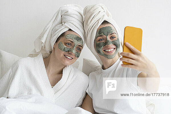 Happy friends wearing facial masks taking selfie through smart phone